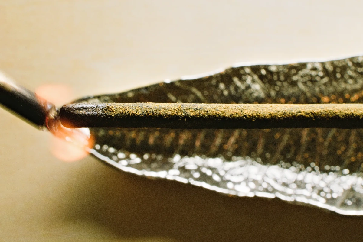 A close up of a stick of incense being lit with a flaming wick.