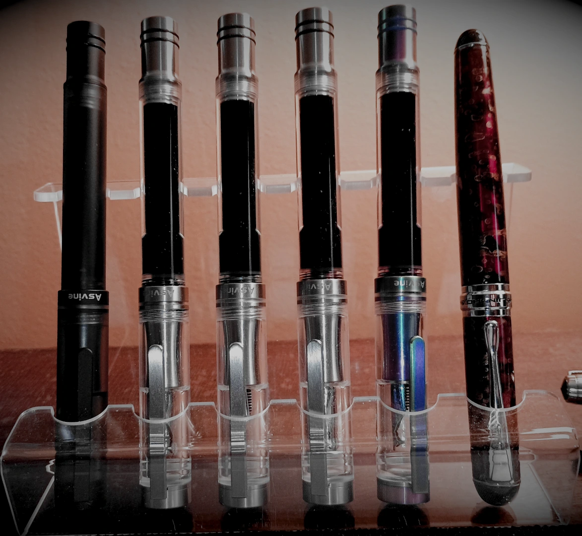 Left to right these pens are filled with Diamine Jet Black, Oxford Blue, Aurora Borealis, Writer's Blood and Imperial Purple inks. To their right is the Jinhao x750 filled with Wordsworth & Black Lavender Purple.