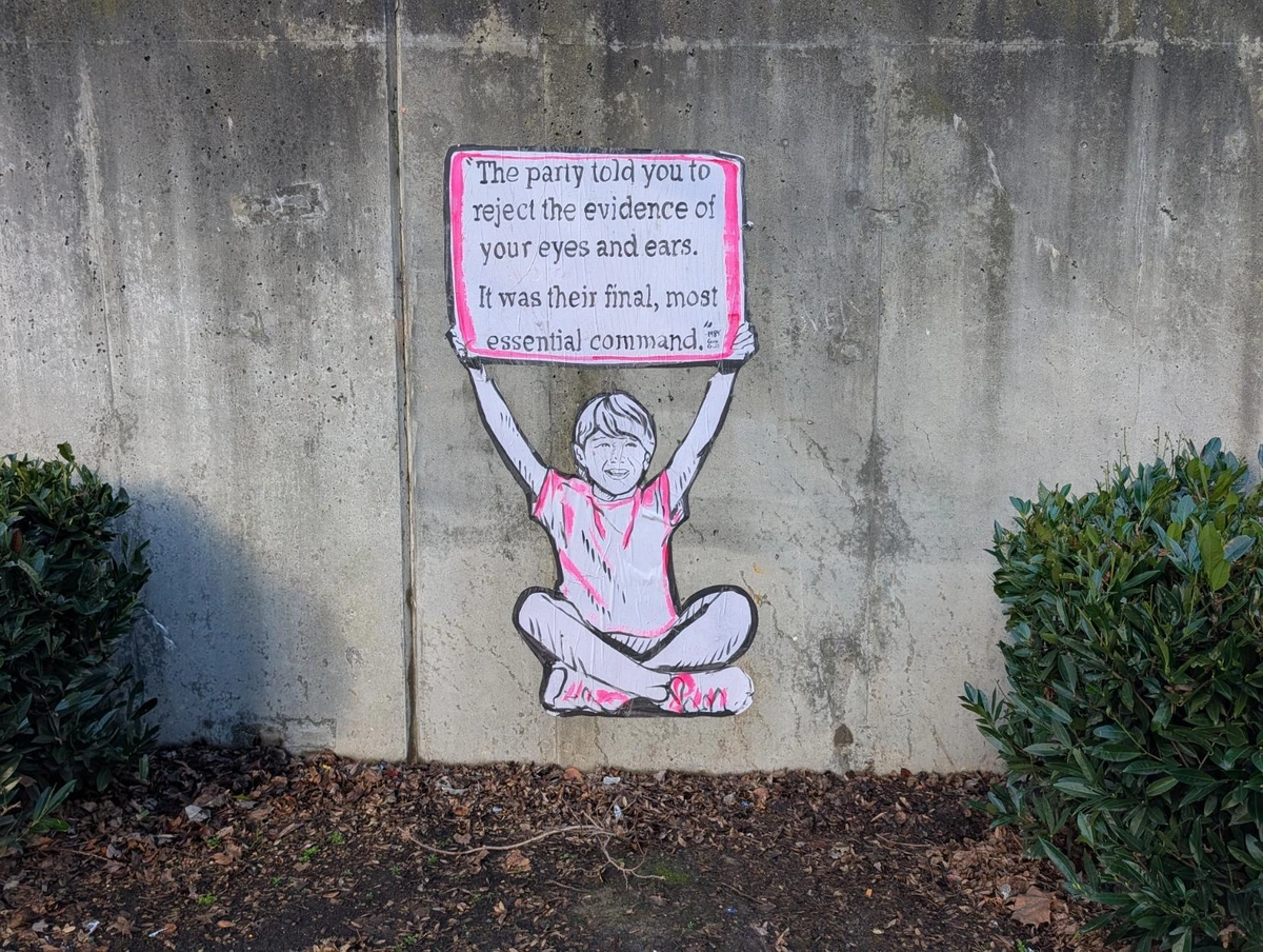 A concrete wall with a paste-up image of a child holding up a sign. The sign reads: "The party told you to reject the evidence of your eyes and ears. It was their final, most essential command."